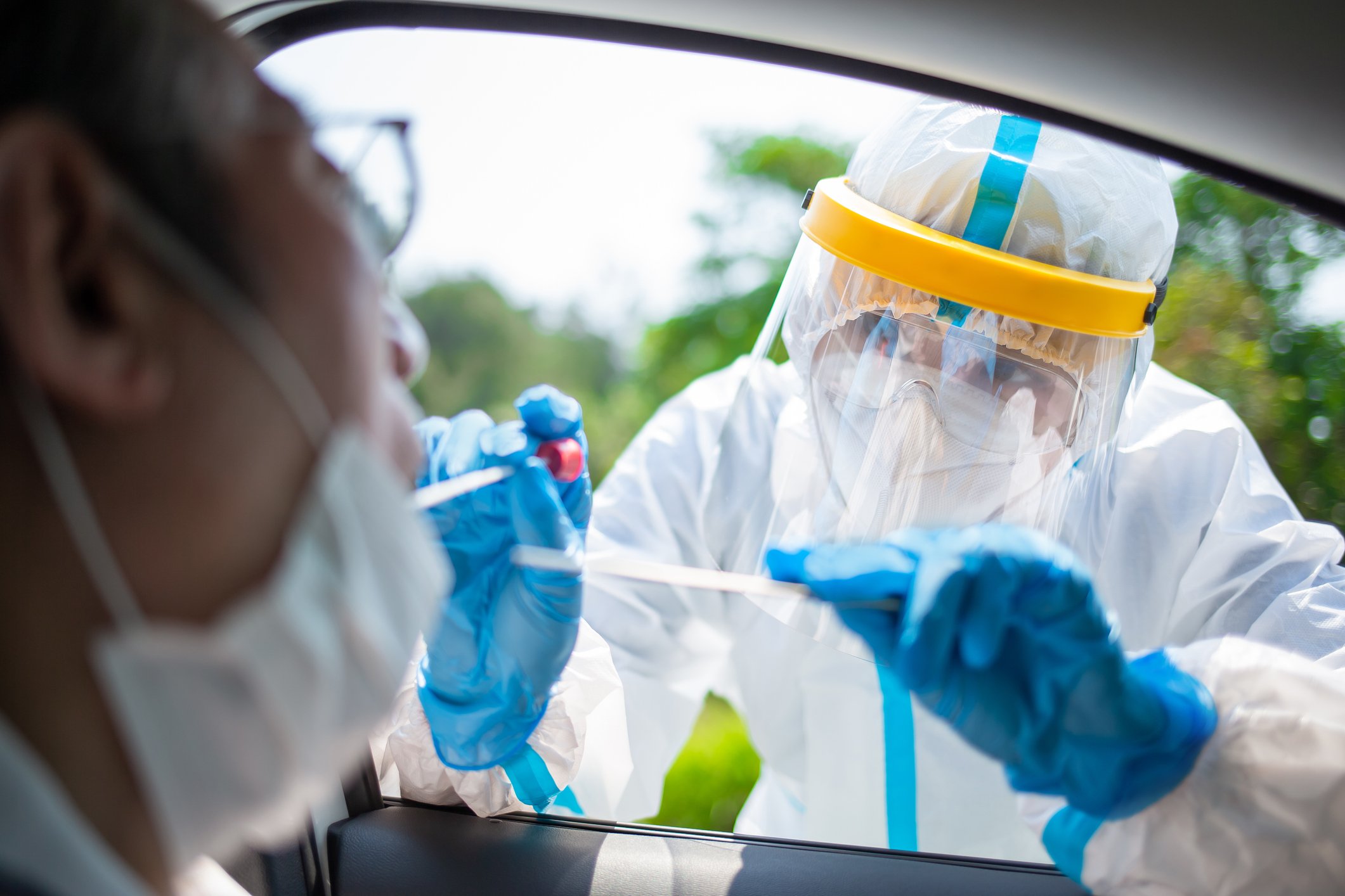 A healthcare worker reaches into a vehicle to take a nasal swab from the driver.