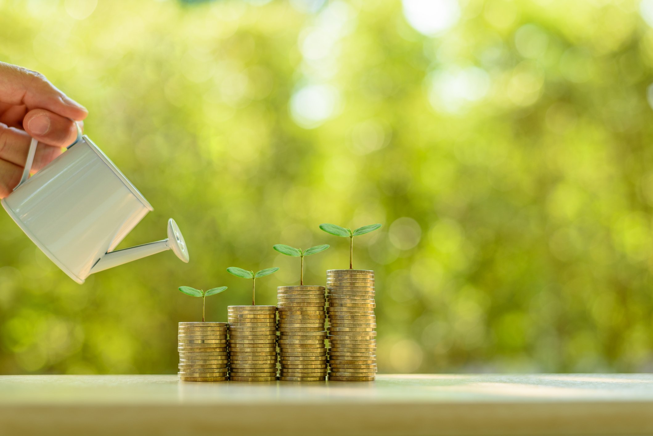 Person watering ascending stacks of coins with little plants growing from them.