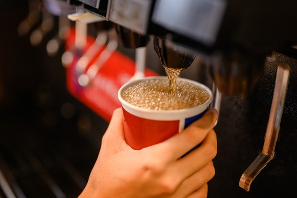 Close-up of a cup being filled with soda at a self-serve fountain.