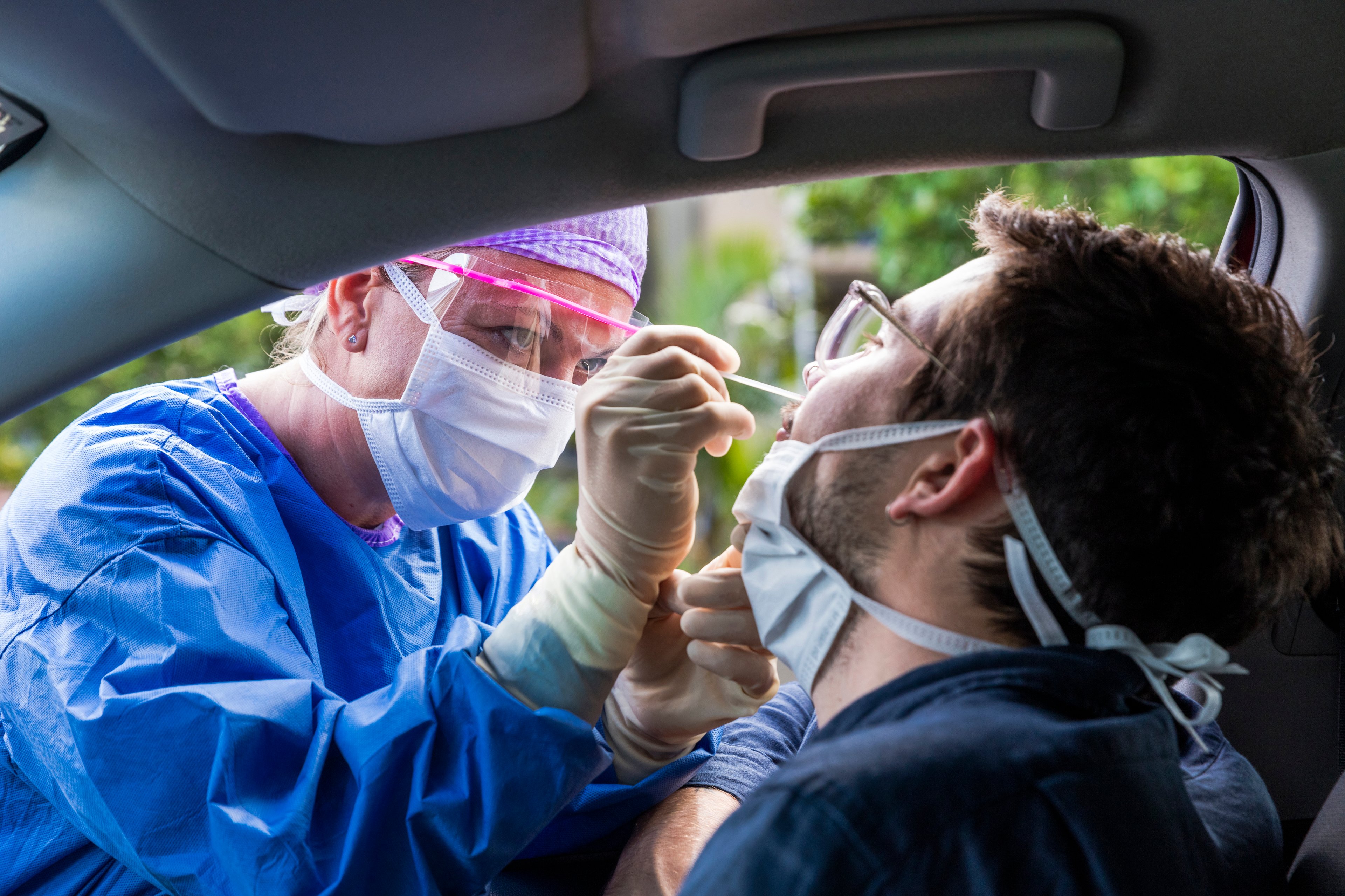 Technician administers a nasal swab coronavirus test to a man sitting in his car.