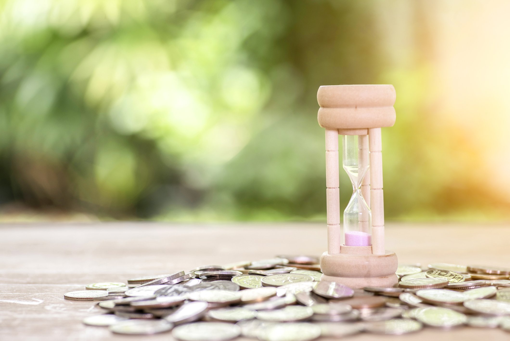 Pink hourglass with coins scattered around it. 
