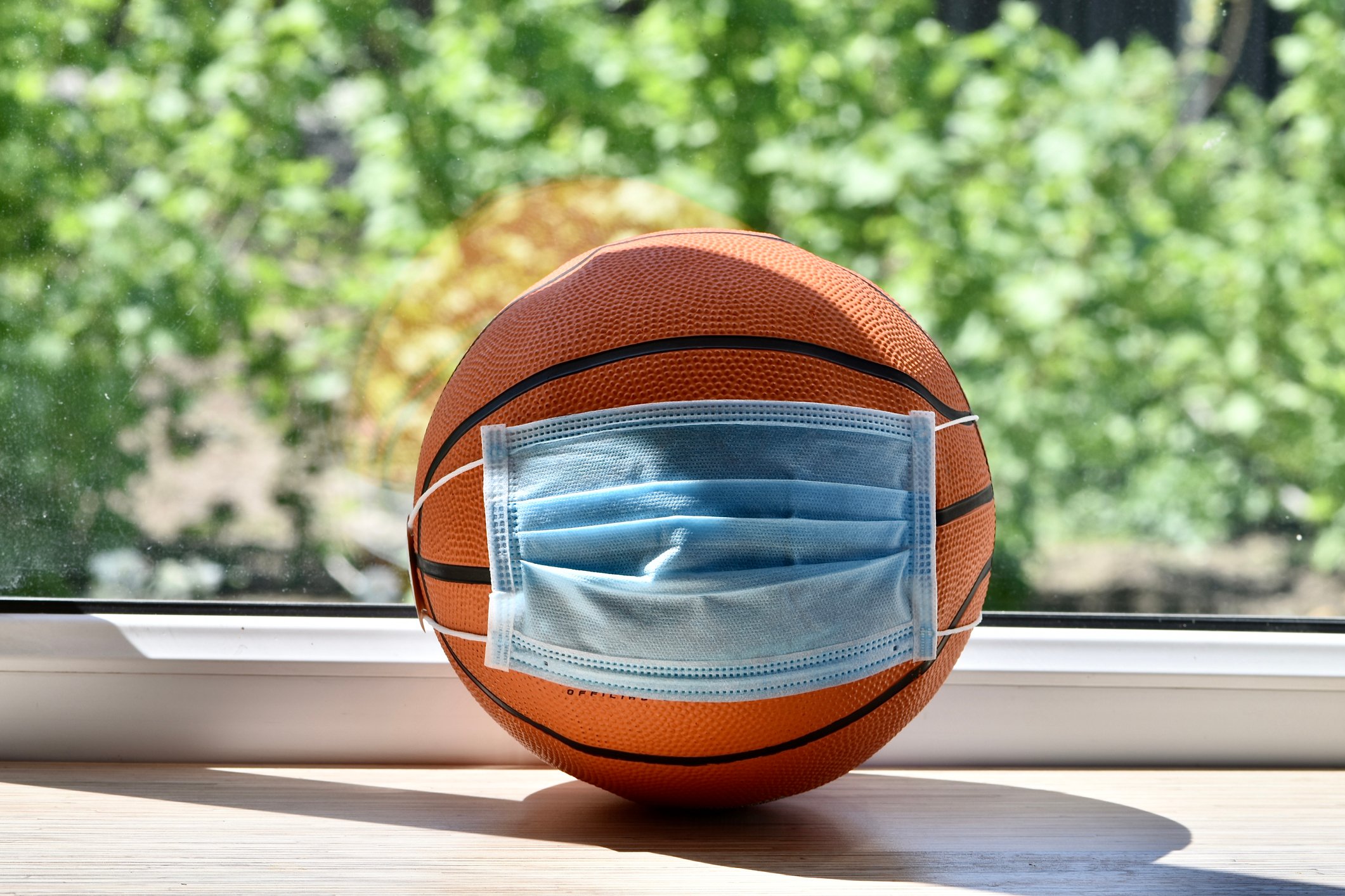 A basketball wearing a blue mask, on a tablein front of a window