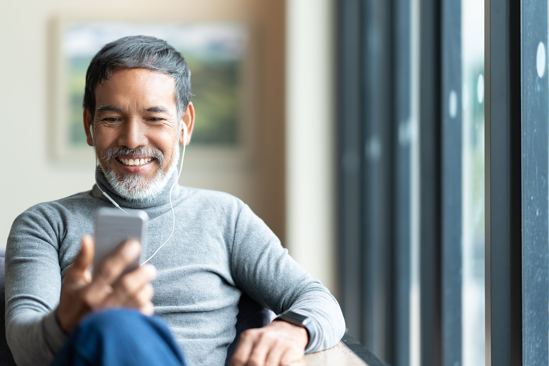 A man listens to his digital music player while sitting in a home on a chair