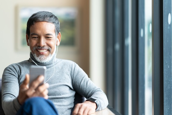 A man listens to his digital music player while sitting in a home on a chair