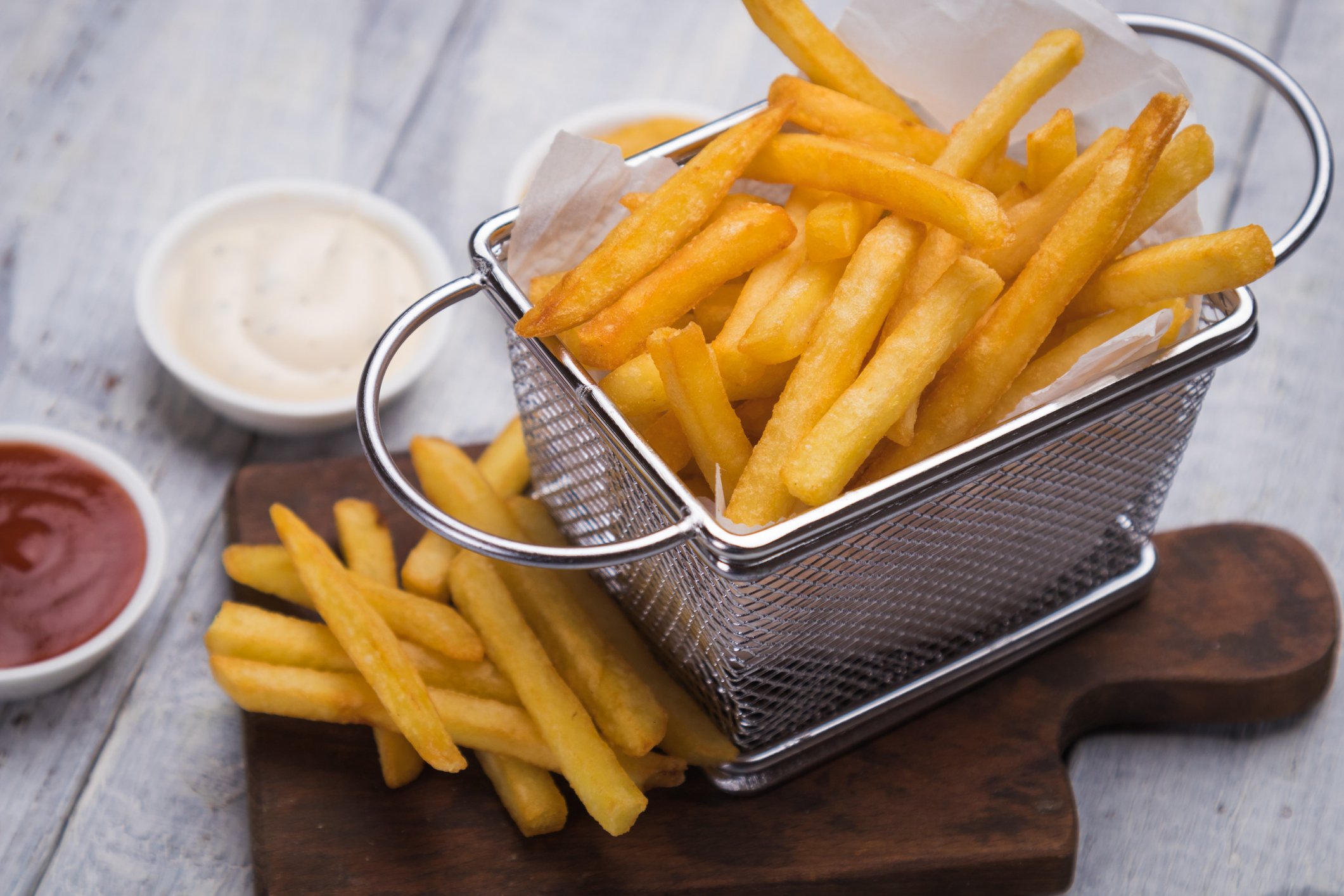A metal basket of French fries atop a wooden cutting board.