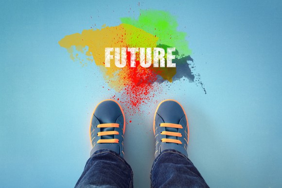 A pair of children's shoes standing in front of the word "future," written in brightly colored powder.