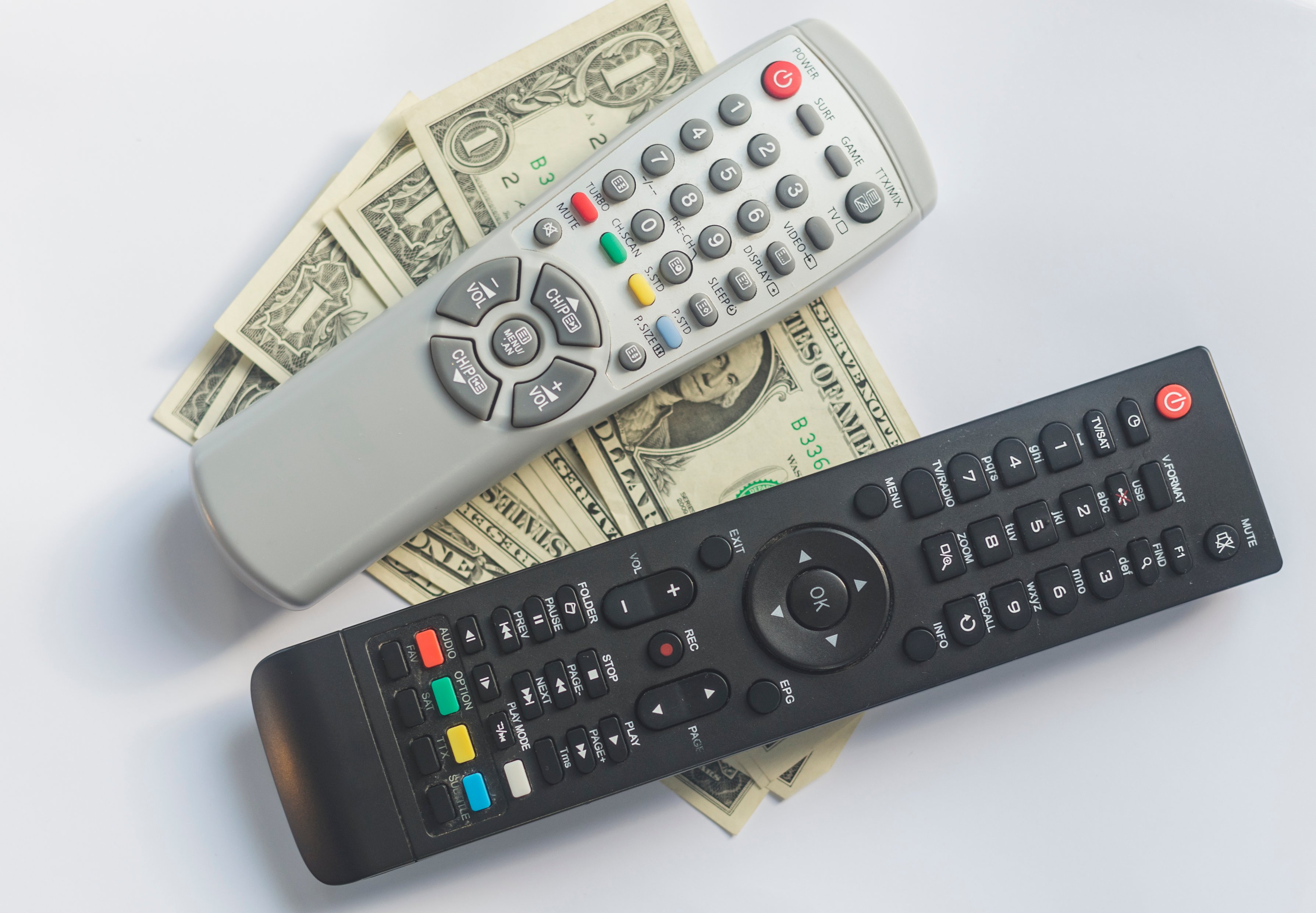Two TV remotes resting on a stack of dollar bills.