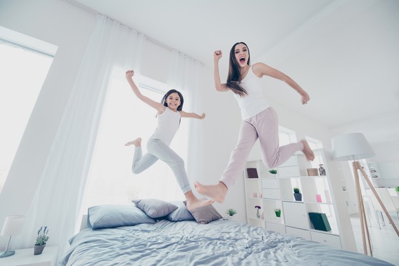 Two people jumping over a bed, with happy faces.
