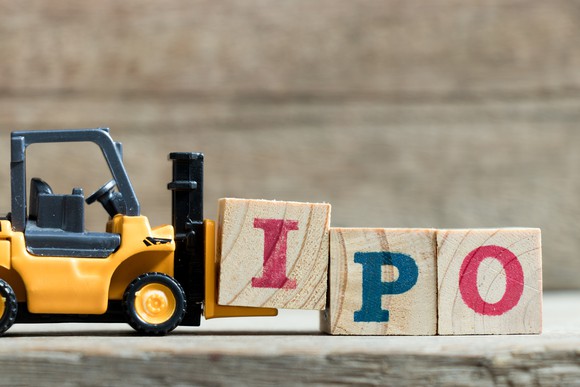 A miniature forklift moves three wooden blocks with the letters "IPO" written on them.