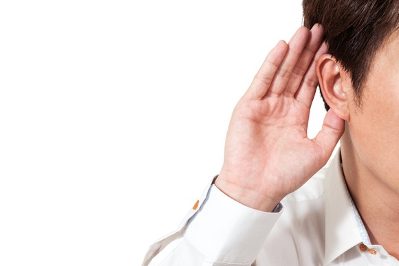 A businessman listens intently, cupping one hand to his ear.