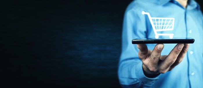 A man holding a phone displaying a shopping cart icon.