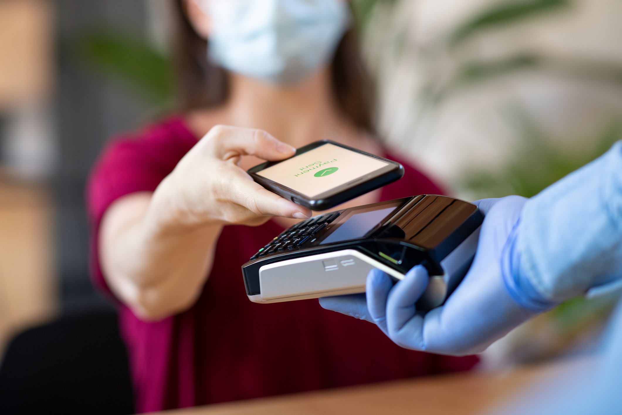 A woman wearing a face mask holds her phone up  to a digital card reader. 