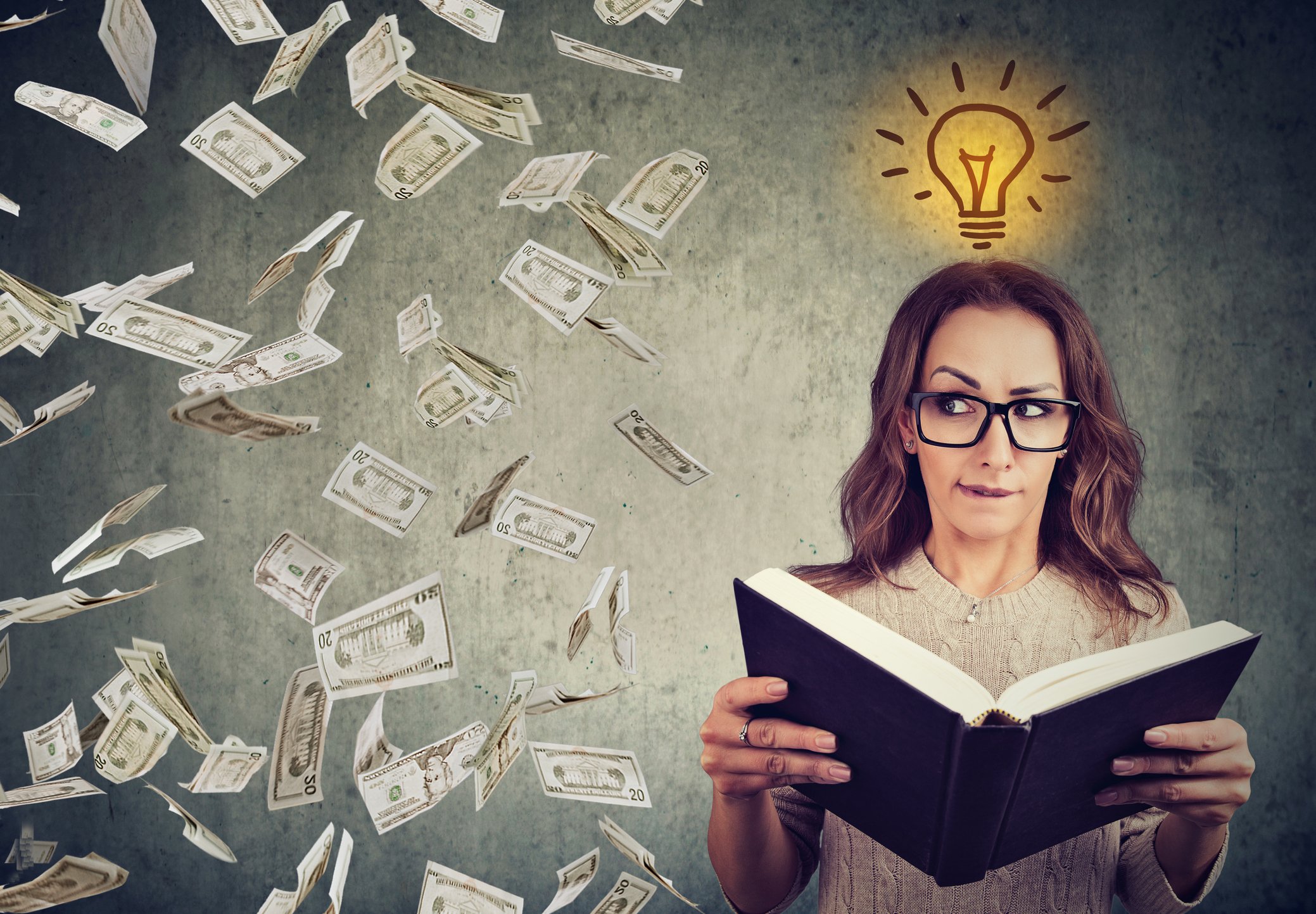 Woman holding book with light bulb and money