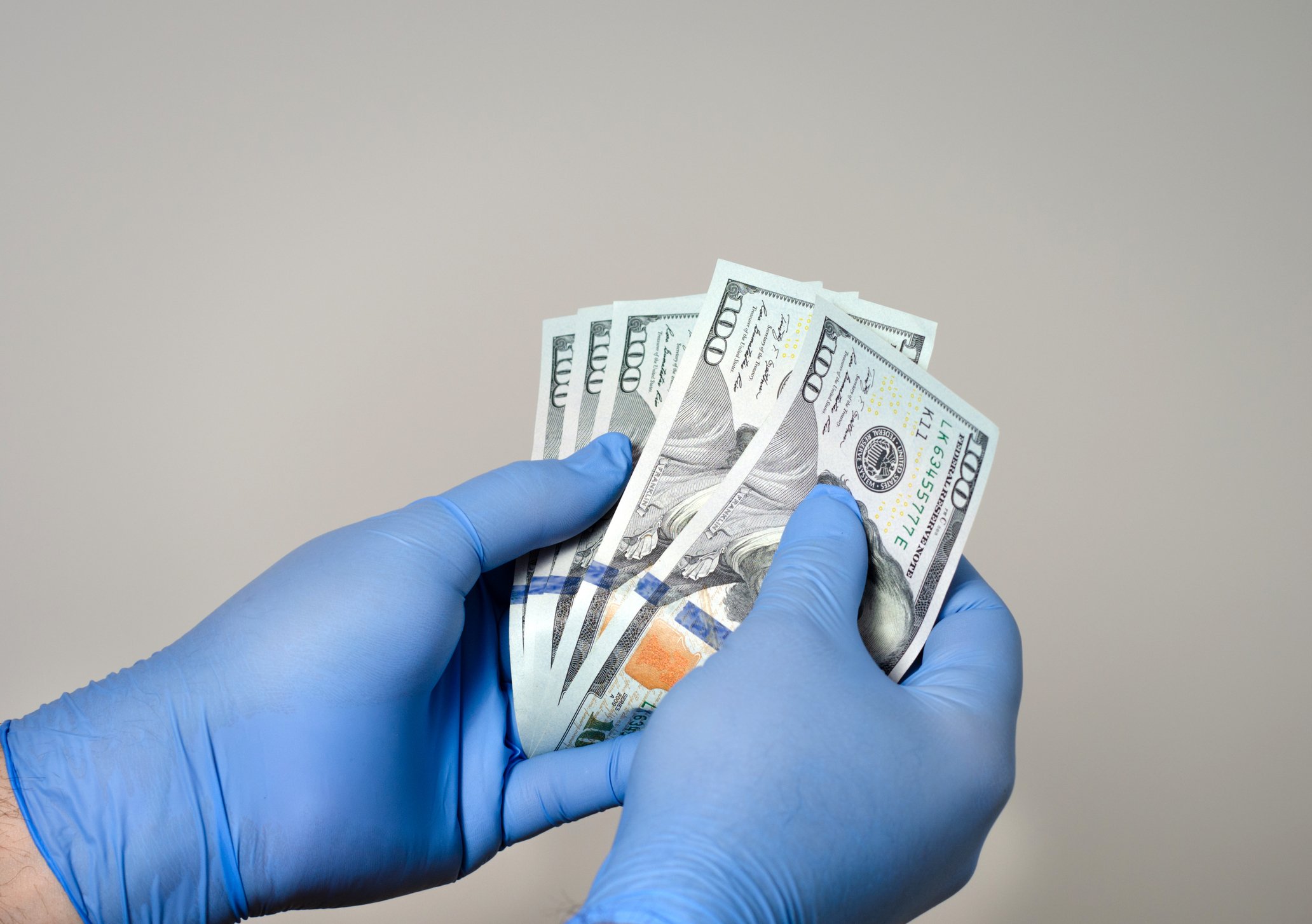 A researcher's gloved hands hold $100 bills. 