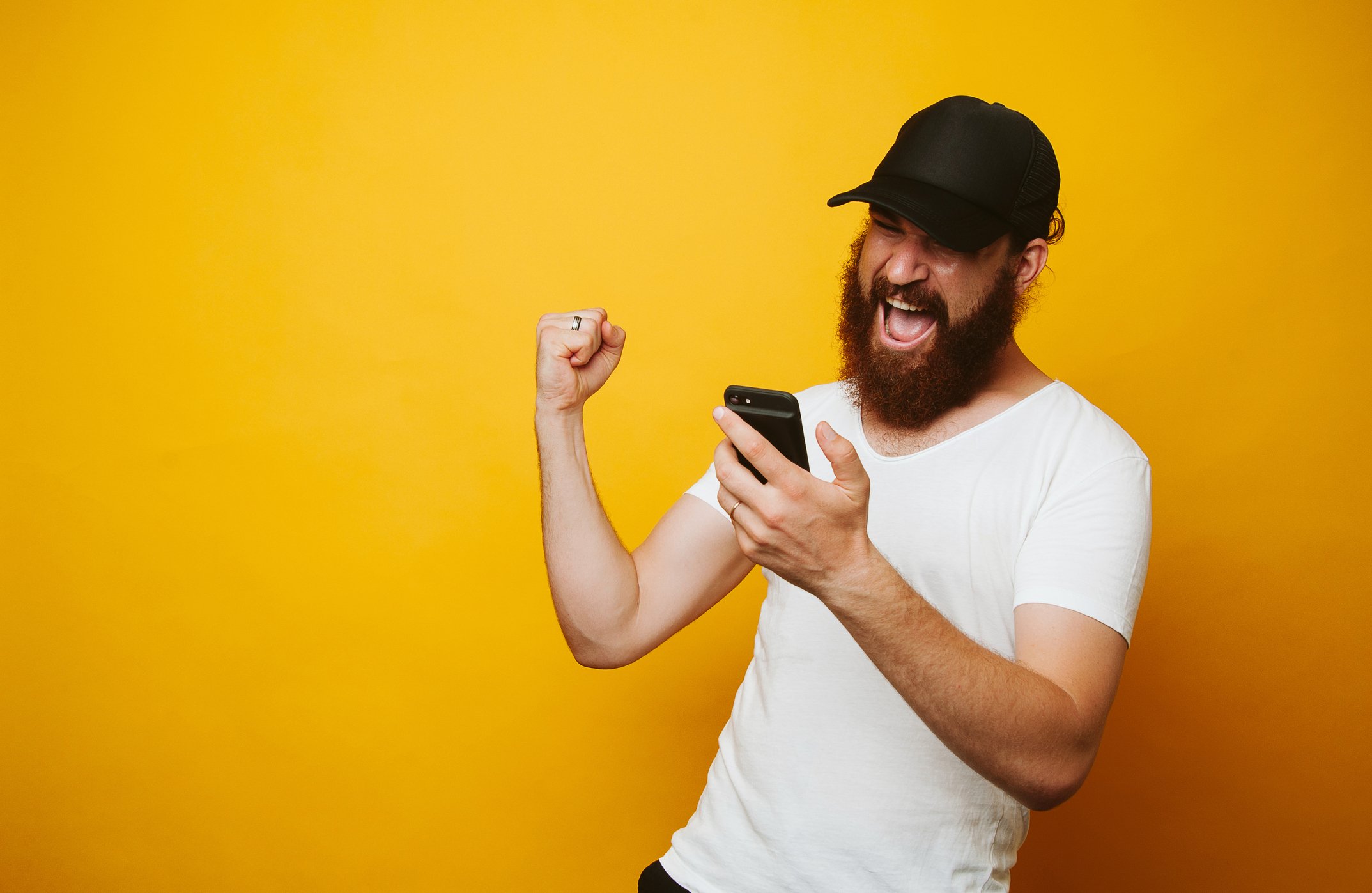 A bearded sports bro pumps his fist and smiles at his phone. 