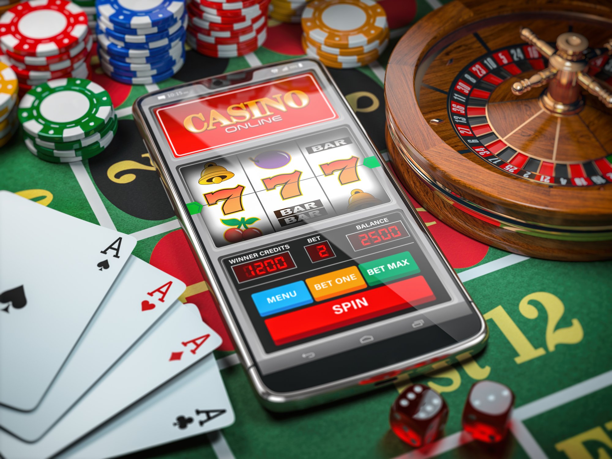 A smartphone with a casino website lying amid dice, cards, poker chips, and a mini roulette wheel.
