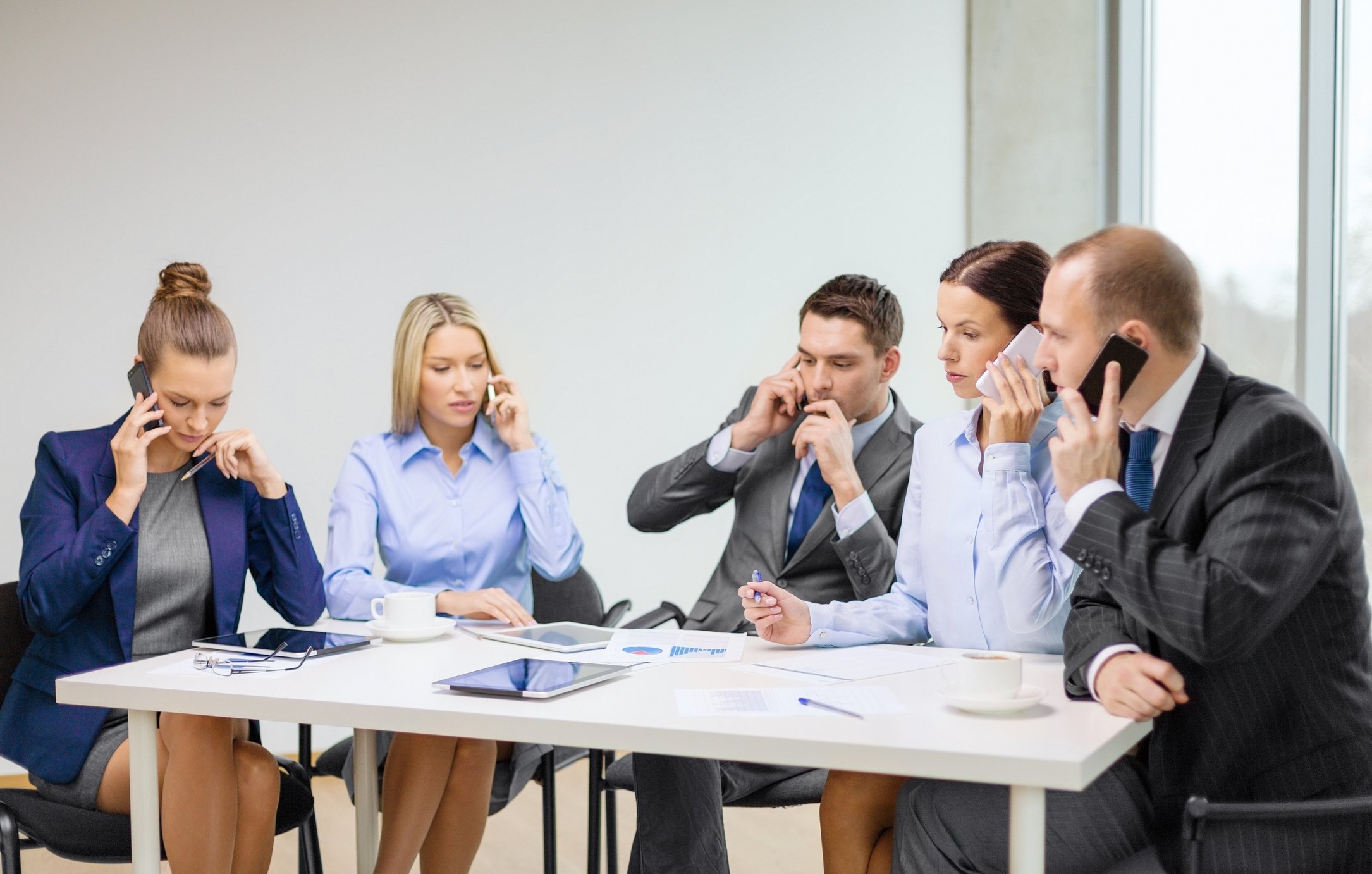 Several people sitting around a table talking on their phones.