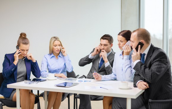 Several people sitting around a table talking on their phones.