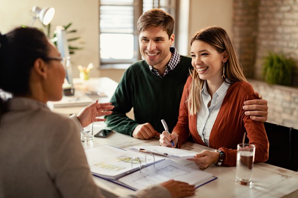 A smiling couple sitting in an office and signing paperwork.
