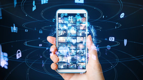 A hand holds a smartphone surrounded by floating digital icons.  