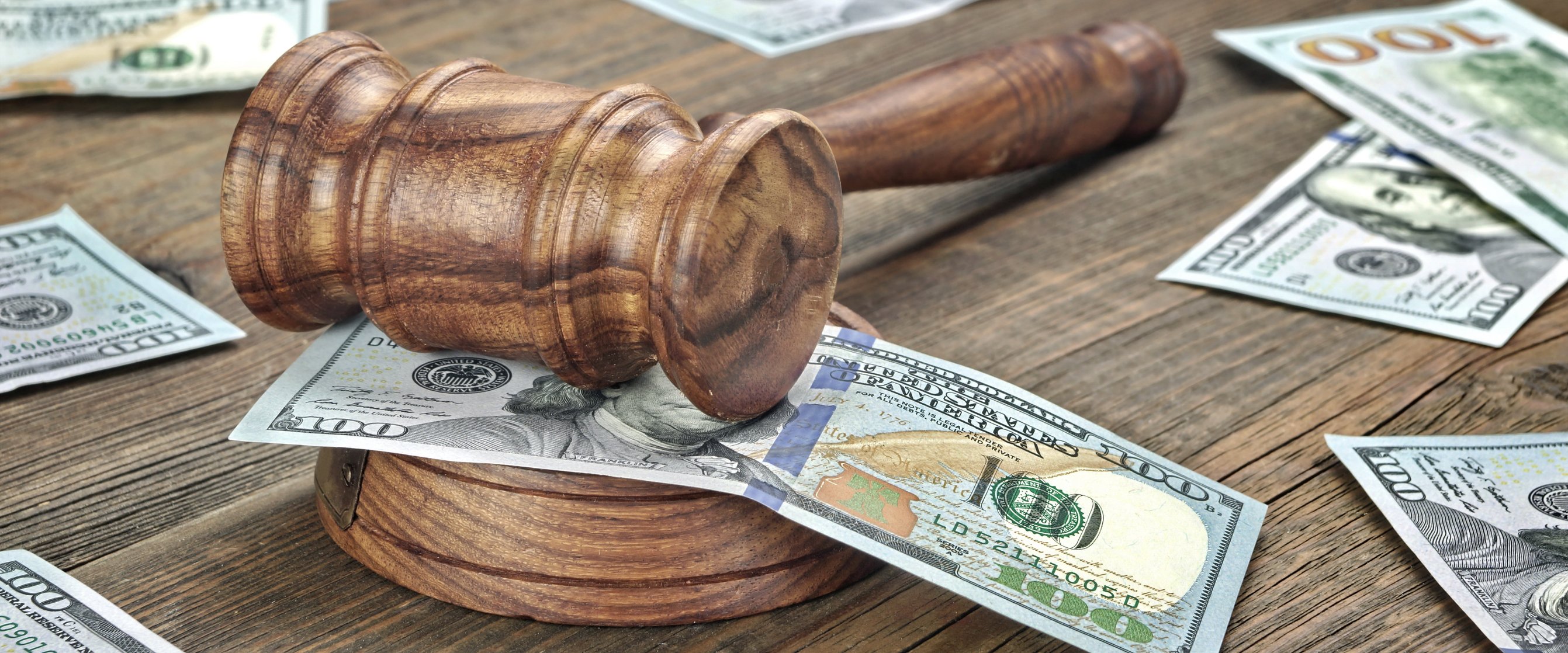 A judge's gavel on a desk covered by one hundred dollar bills. 