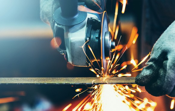 A worker grinds a steel tube in a machine shop. 