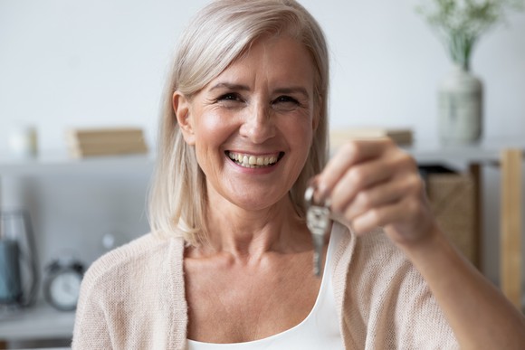 Older woman smiling holds out house key.
