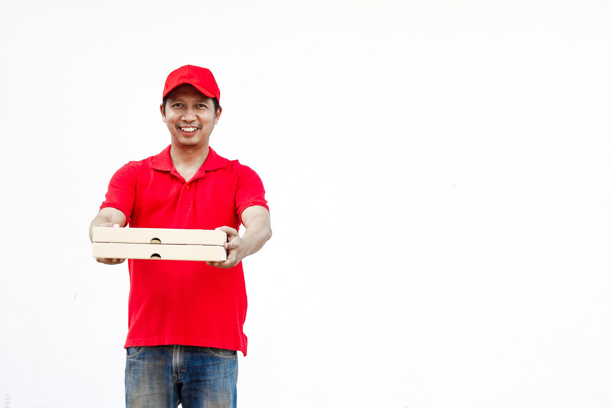A man in a red shirt and hat is holding two pizza boxes.