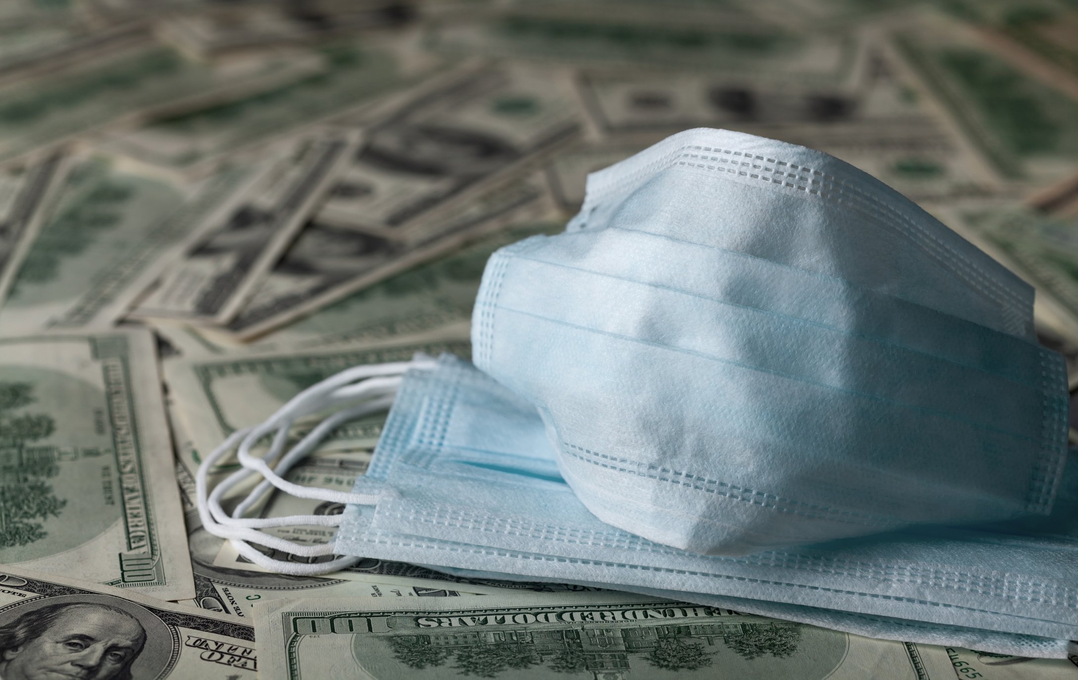 A hospital mask is pictured on top of a pile of $100 bills.