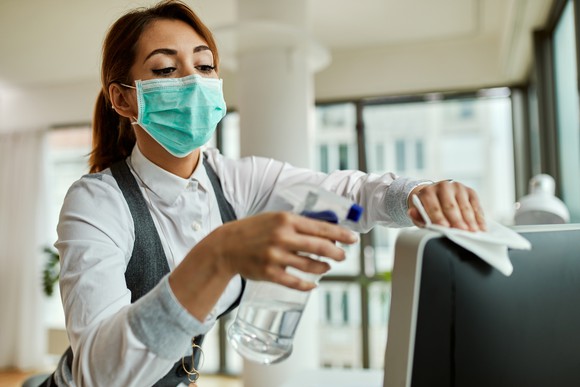 A woman wearing a mask cleans a television set. 