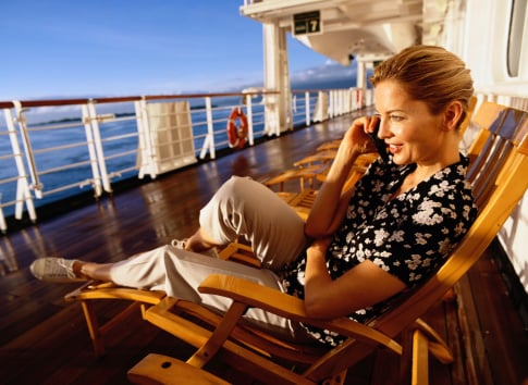 A lady relaxing on an outdoor cruise deck while on the phone.