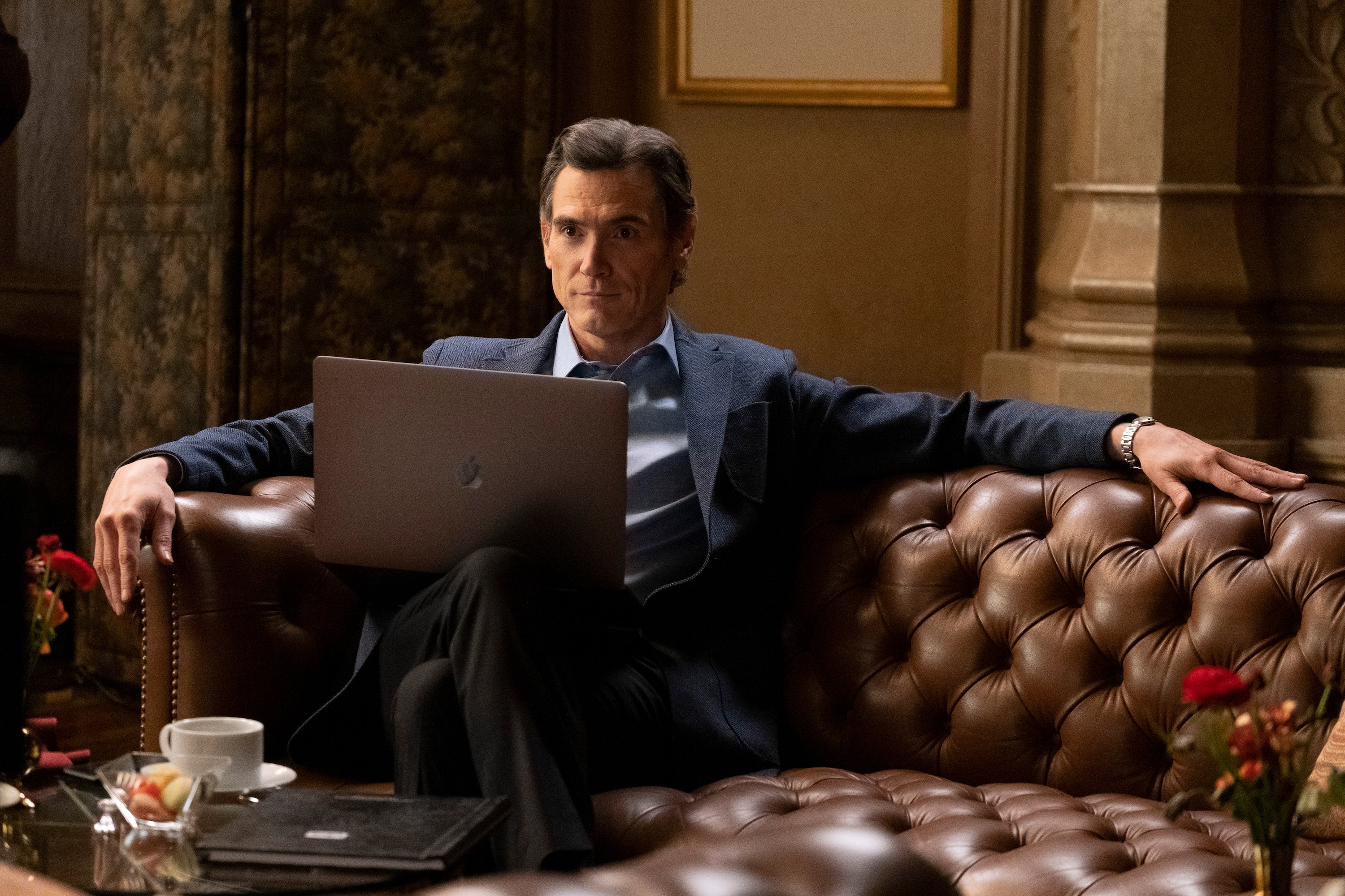 Billy Crudup sitting on a couch with a MacBook