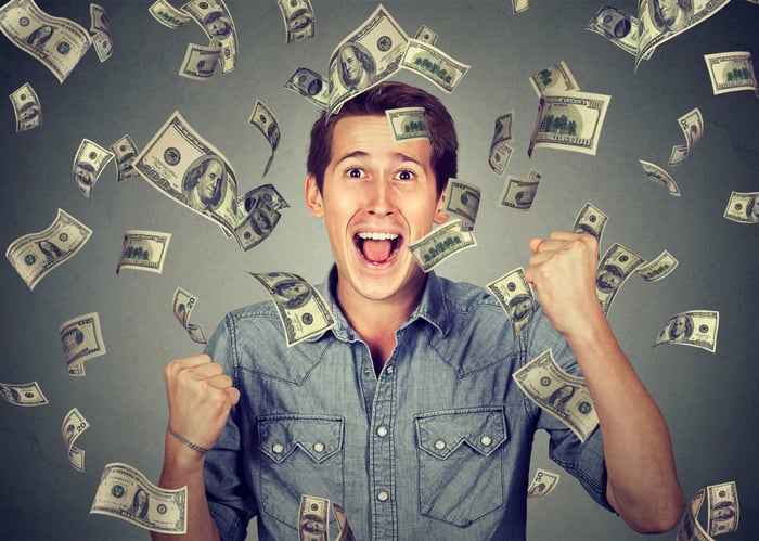 Dollar bills showering down while a man cheers. 