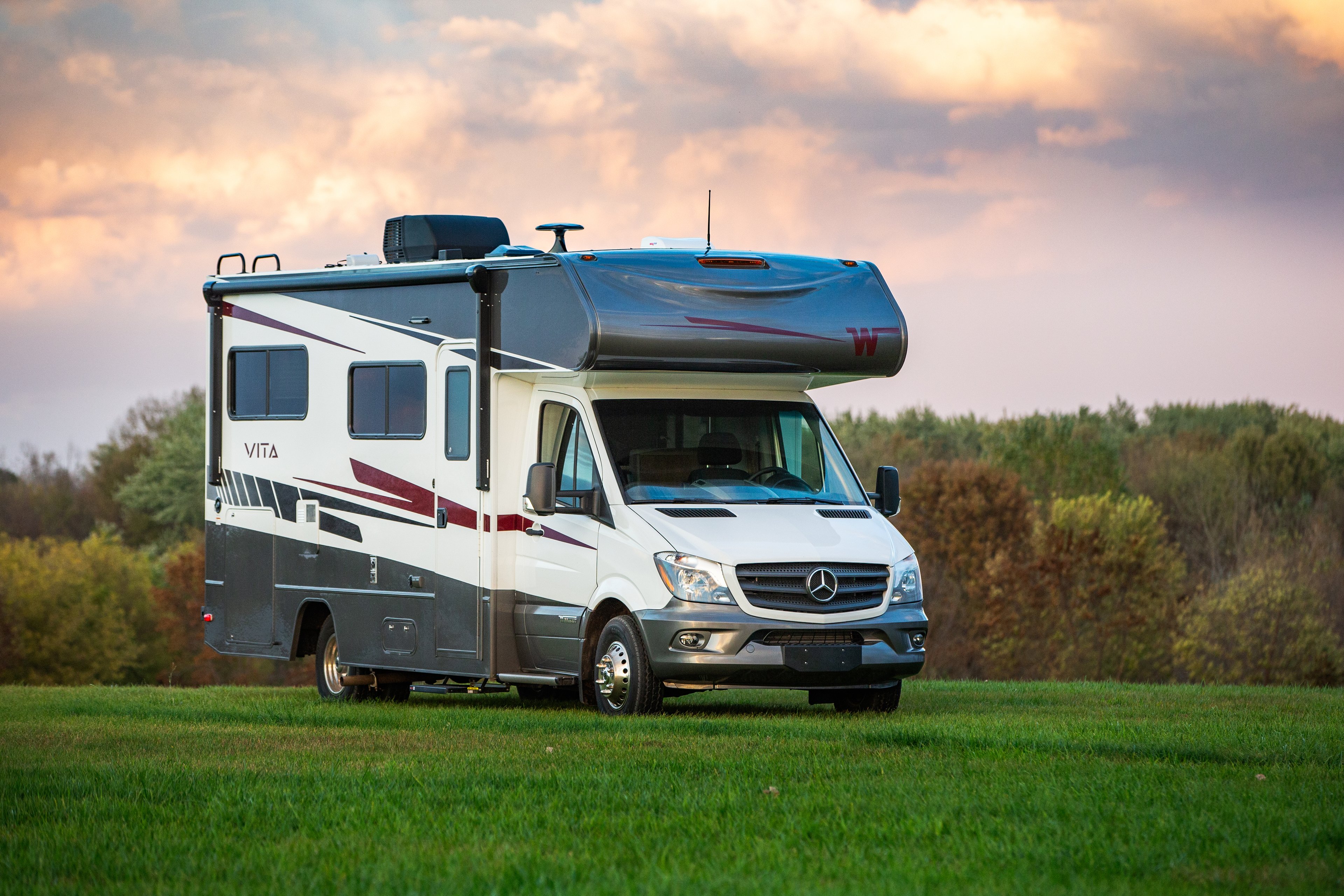 The Winnebago Vita model recreational vehicle sits out in a field under a cloudy sky.