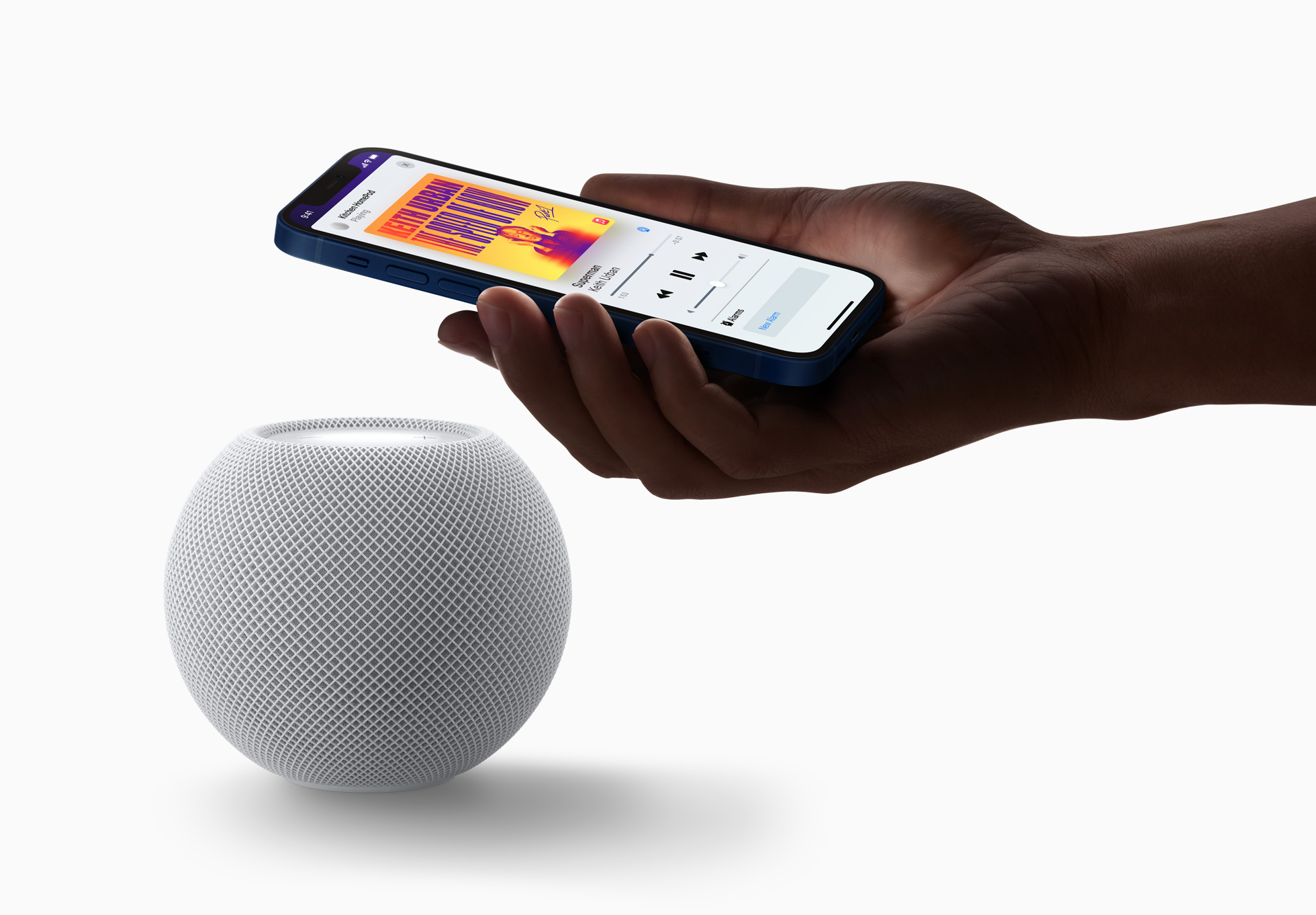 Hand holding an iPhone next to the HomePod Mini