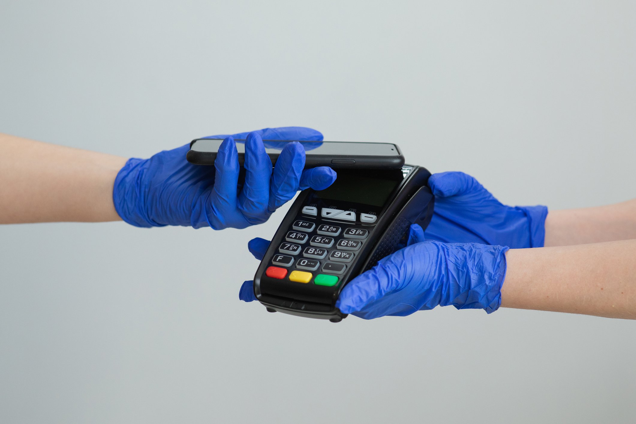 A person wearing protective glove paying with his phone while a person in gloves is holding a payment processing device. 