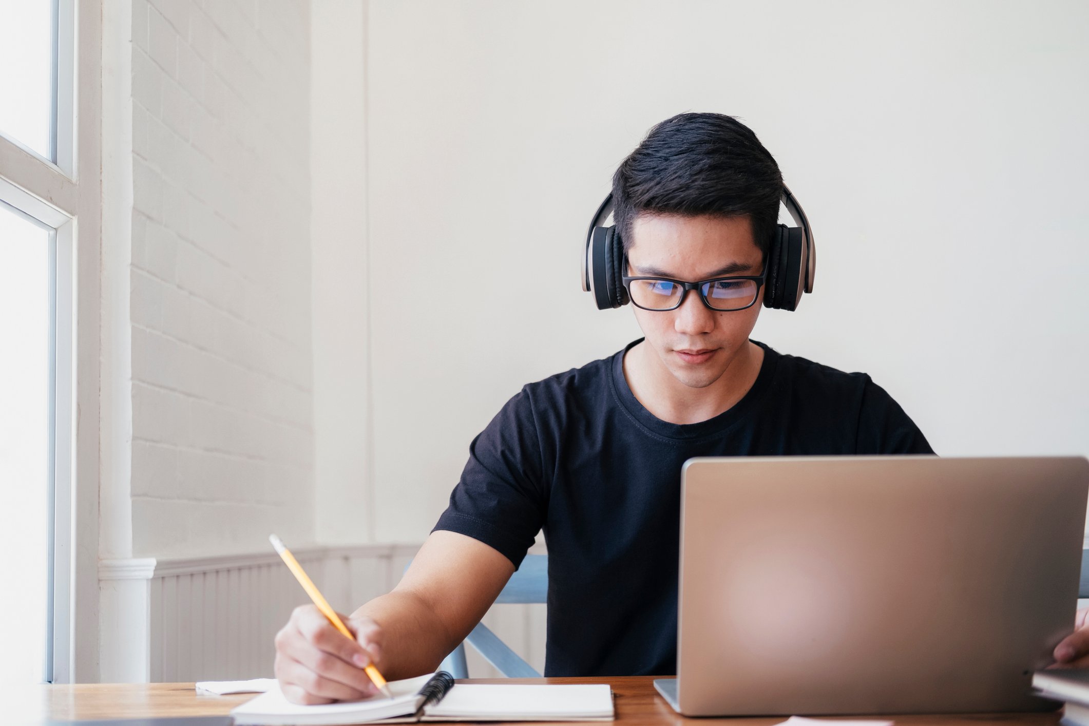 A student sitting at a desk with a laptop taking notes. 