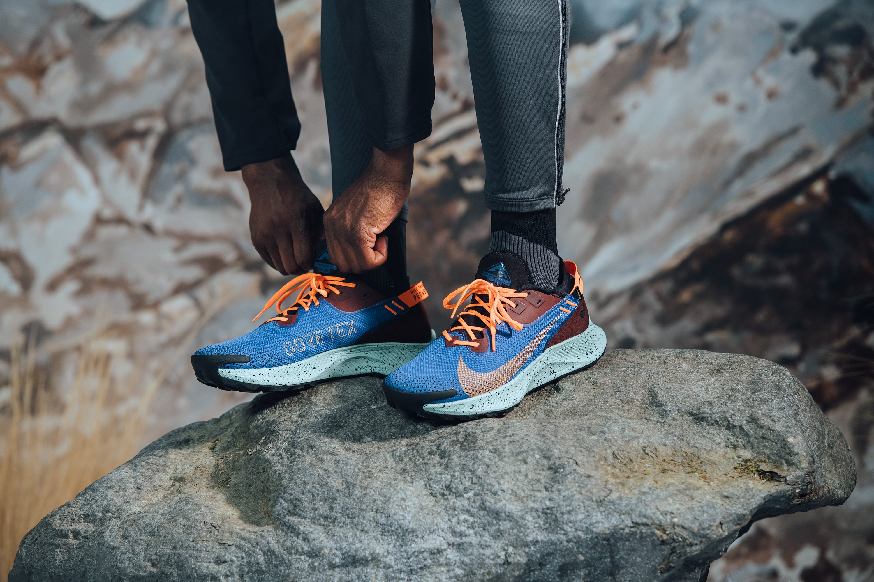 Close-up of person leaning down and adjusting their Nike sneakers while standing on a rock