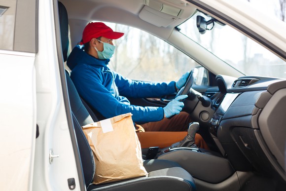 masked food delivery driver with package on passenger seat