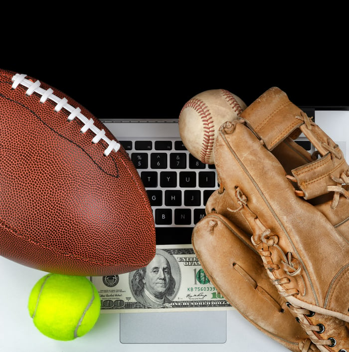 A football, baseball, and baseball glove on a keyboard, with a $100 bill.