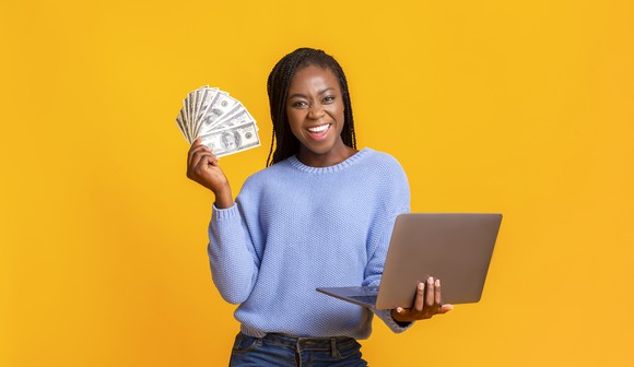 Woman holding laptop and dollar bills. 