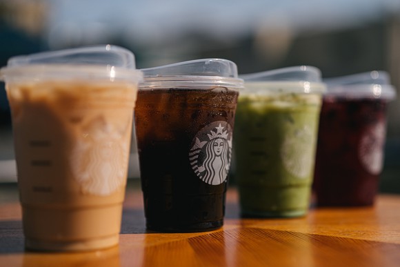 Four cups holding Starbucks drinks are lined up and feature plastic lids.