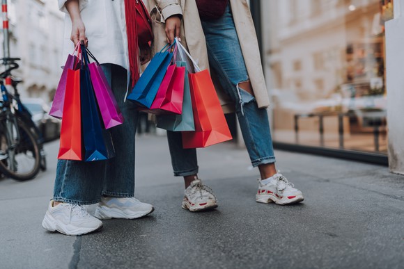 Two women holding shopping bags on a sidewalk.