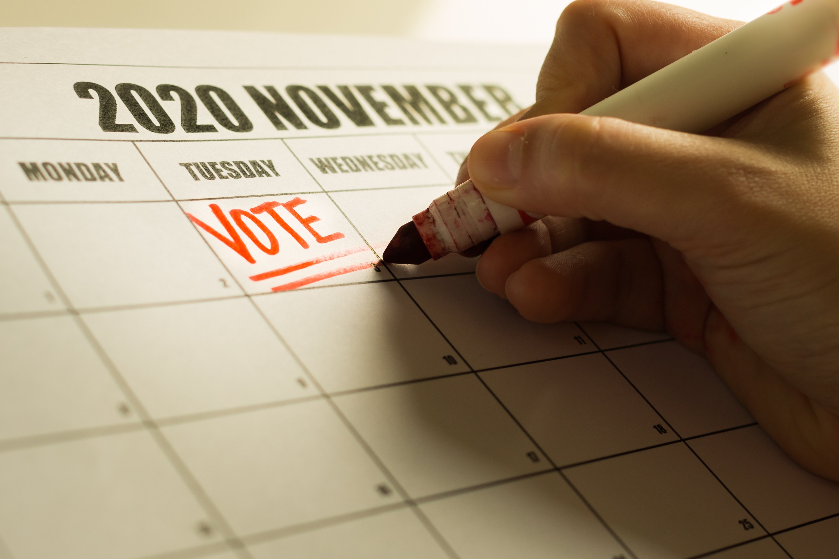 A hand writing the word VOTE on Tuesday the 3rd on a calendar showing November 2020