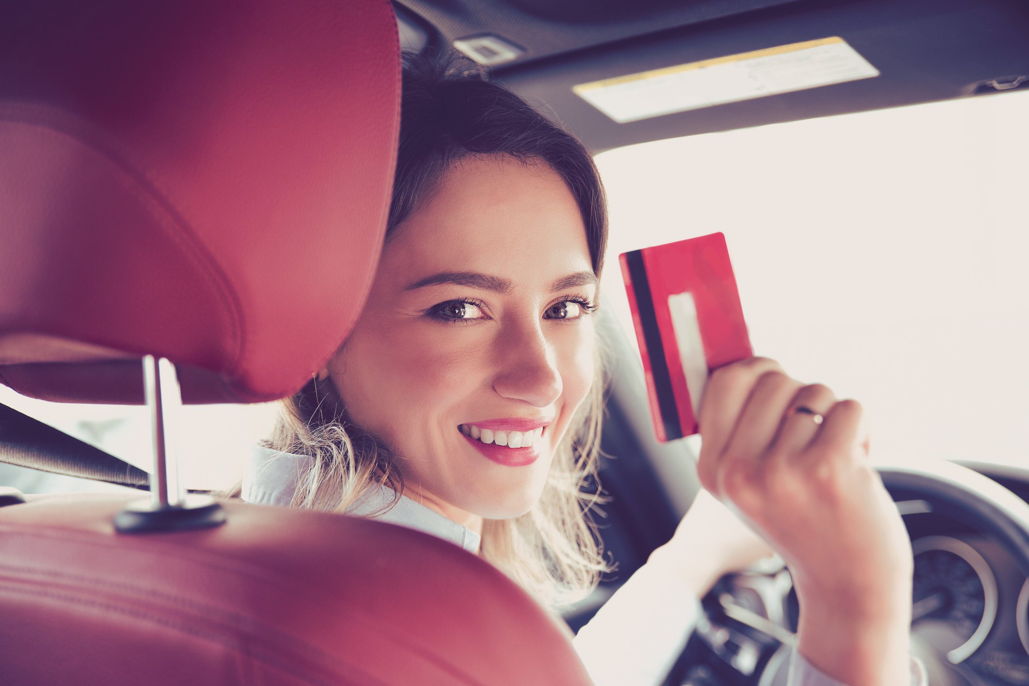 A woman in a driver seat happily flashing a payment card.