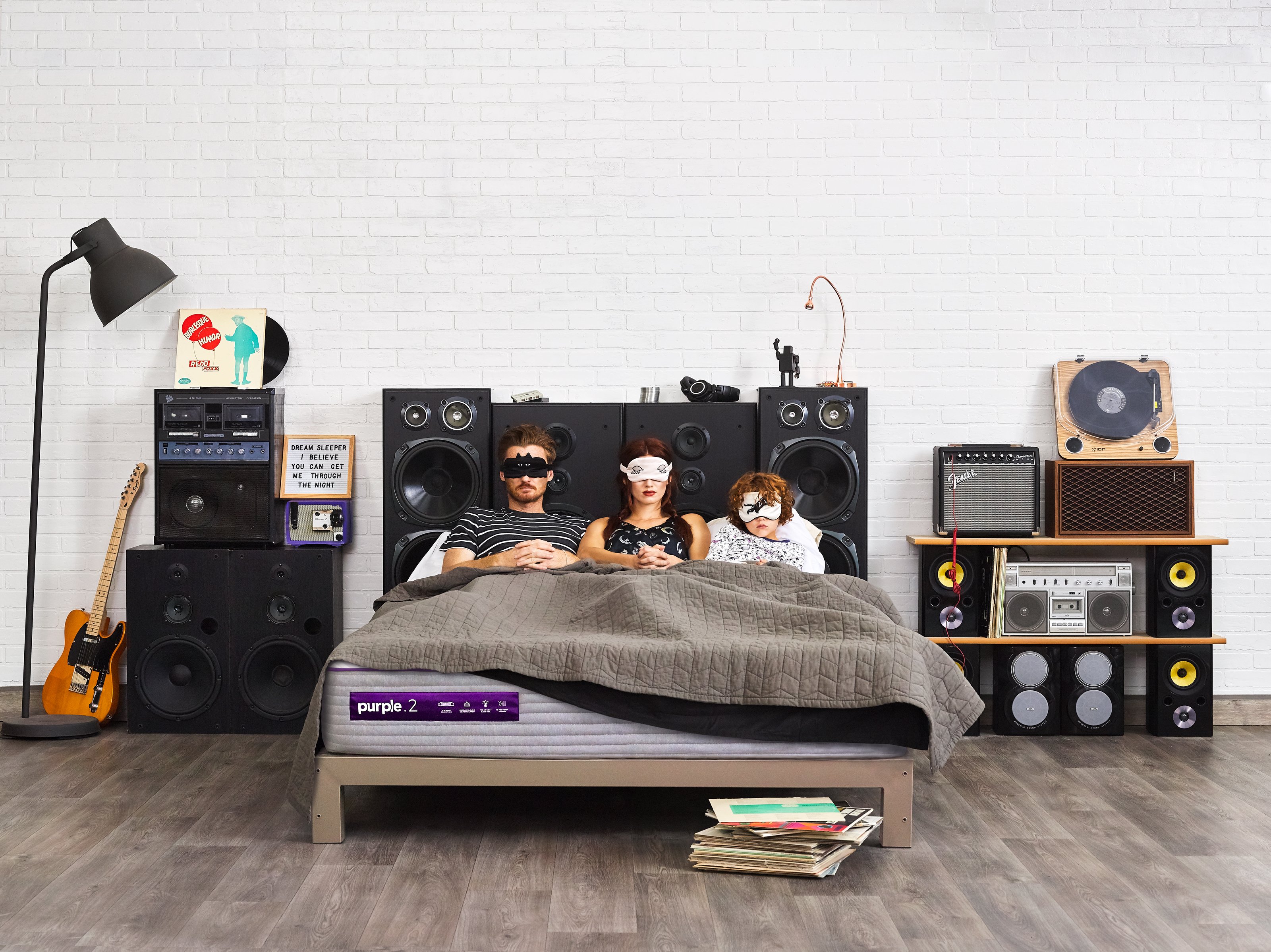 Three people wearing masks lay on a mattress from Purple Innovation in a bedroom setting.