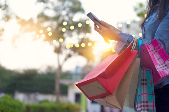 A shopper checks her phone while holding shopping bags.
