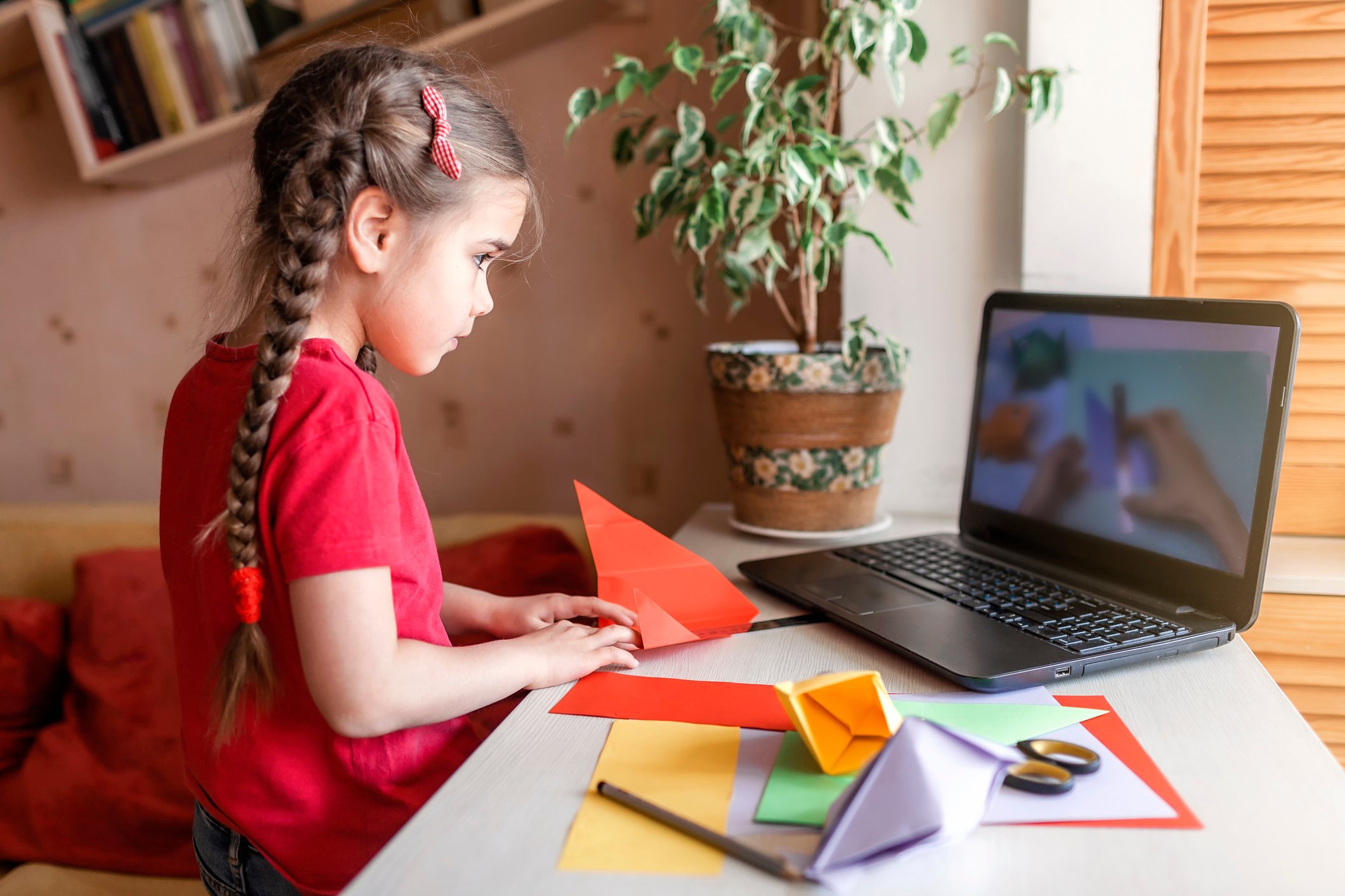 A girl looking at a laptop while folding a piece of paper.