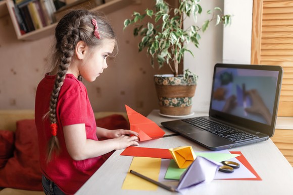 A girl looking at a laptop while folding a piece of paper.