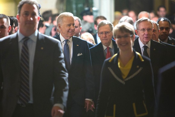 Joe Biden walks with other legislators down a hall. 